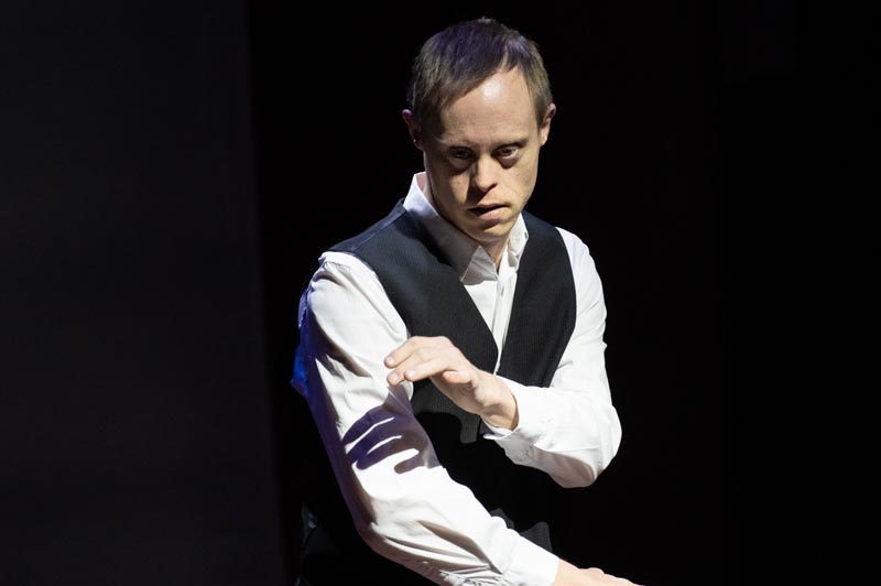 Joel Forman performing. He is wearing a white shirt and black waistcoat